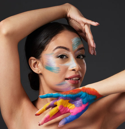 Woman, portrait and beauty with rainbow paint art on hand and face in studio with a smile. Creative...