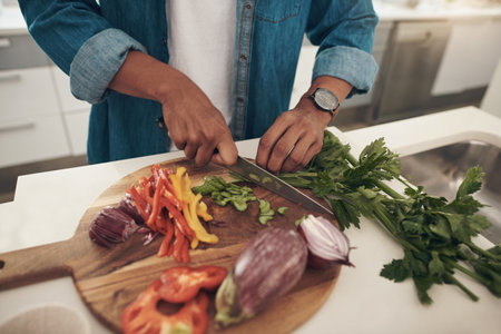 Prepping for a healthy dish. Closeup shot of an unrecognisable man chopping vegetables while cooking at home.の写真素材