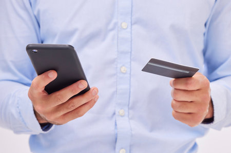 Man, ecommerce with smartphone and credit card in hands, closeup with fintech and online shopping isolated on white background. Payment, internet banking and technology, bank app and male in studioの写真素材