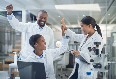 Science causes all kinds of crazy reactions. a group of young scientists giving each other a high five while using a laptop in a laboratory.の写真素材