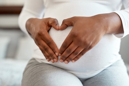 In love with a human I havent met yet. Closeup shot of an unrecognisable woman making a heart shape with her hands on her pregnant belly at home.の写真素材