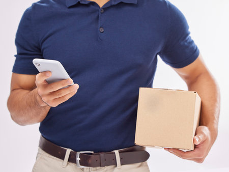Delivery man with package in hands, phone and box, ecommerce and shipping isolated on white background. Communication, fintech and zoom, digital invoice and male in studio with commercial serviceの写真素材