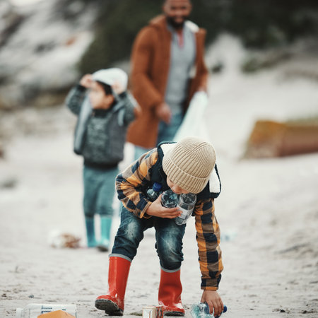 Beach clean, plastic and pollution with a child cleaning the environment for dirt or bottle on sand. Male kid and family walking as volunteer for sustainability, community service and global warmingの写真素材