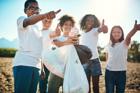 We care for the earth so we keep it clean. a group of teenagers picking up litter off a field and showing thumbs up at summer camp.の写真素材