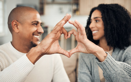 Love, happy and hand heart by couple on sofa with love, care and trust at home together. Emoji, shape and man with woman hands in support of hope, marriage and unity, smile and joy in living roomの写真素材