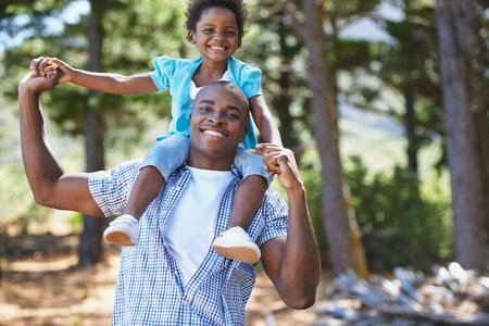 Teaching his little girl about nature. Portrait of a father carrying his daughter on his shoulders while enjoying a day outdoors.の写真素材