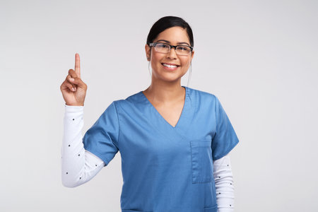 Sleep off the pain, well try again. Portrait of a young doctor wearing glasses and scrubs, pointing up against a white background.の写真素材
