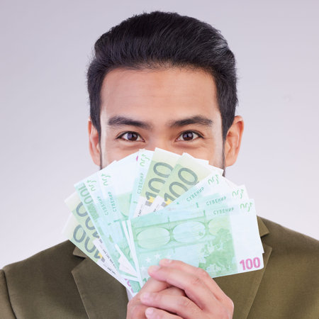 Portrait, cash and euro with a business man in studio holding money on a gray background for...