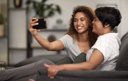 We are making photographs to understand what our lives mean to us. a lesbian couple taking a selfie of the couch at home.の写真素材