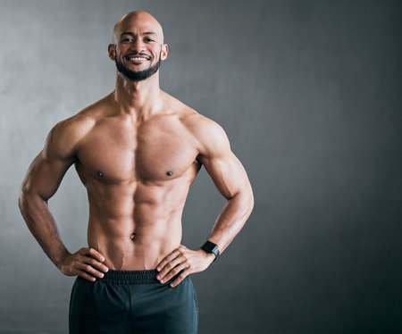 Built like a gladiator. Cropped portrait of a handsome young male athlete standing shirtless with his hands on his hips against a grey background.の写真素材