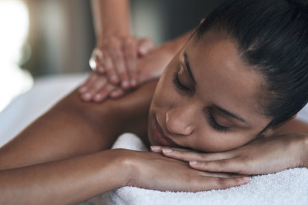 When your body feels tense, loosen up at the spa. a young woman getting a back massage at a spa.の写真素材