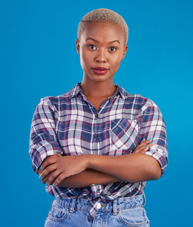 Serious, confidence and portrait of black woman with crossed arms, proud and empowerment in studio. Fashion, beauty and attractive girl on blue background with pride, success mindset and motivationの写真素材