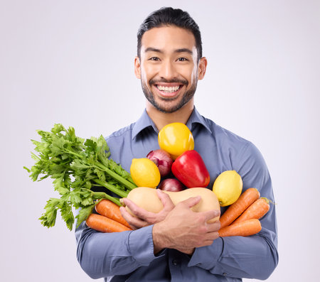 Healthy, happy and portrait of an Asian man with vegetables isolated on a white background in a studio. Smile, holding and a Japanese male with food for a diet, vegan lifestyle and nutritionの写真素材