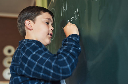 I know all of these answers. a young boy standing alone and writing on the blackboard during a lesson in his classroom at school.の写真素材