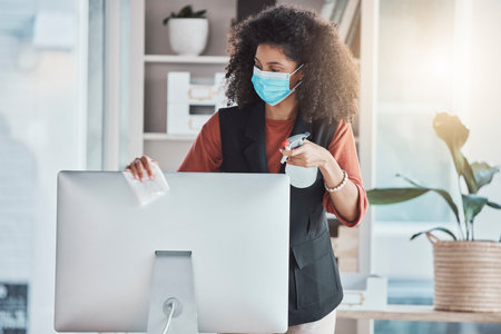 Woman, covid and spray for cleaning computer with face mask, workplace safety and liquid for healthcare. Professional cleaner, desktop pc and clean to stop virus in office with bacteria risk at jobの写真素材