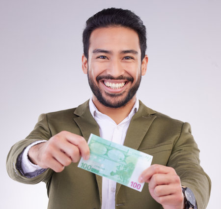Portrait, money and euro with a business man in studio holding cash on a gray background for finance. Smile, accounting or investment with a happy male employee proud of his financial trading successの写真素材