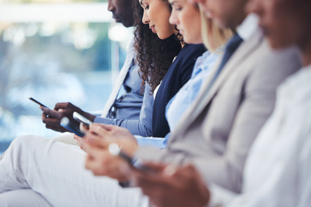 Business people, hiring and hands with phone in waiting room for networking, social media or communication at office. Group of employee workers wait in line or row with smartphone on recruitment appの写真素材