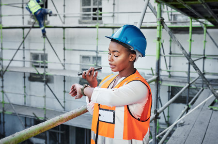 Time delays are not part of this project. a young woman using a smartphone and checking the time while working at a construction site.の写真素材