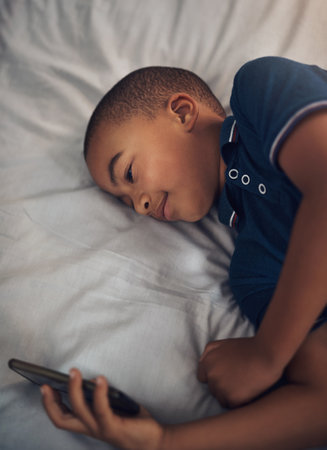 When theres not much to do, theres always something to watch. a young boy using a cellphone while lying on his bed.の写真素材