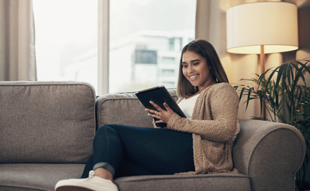 The smartest way to simplify everyday life. a young woman using a digital tablet on the sofa at home.の写真素材