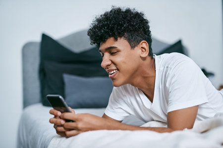 Keeping his social life active in quarantine. a young man relaxing on his bed and using a...