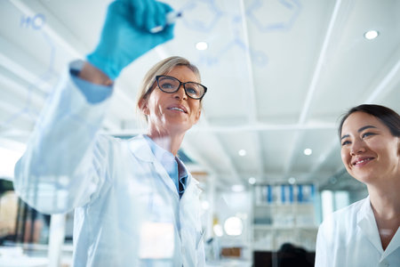 Science can be exciting too. two scientists drawing molecular structures on a glass wall in a lab.