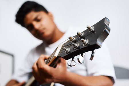 Pick up the guitar and make some music. a young man playing the guitar while sitting at home.の写真素材