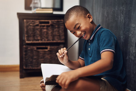 I get to choose who appears in my stories. a young boy writing in a book while sitting at home.の写真素材