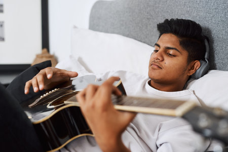 Playing the guitar makes me feel fulfilled. a young man playing the guitar while sitting at home.の写真素材