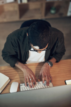 Pouring hours of research into his project. High angle shot of a young businessman using a computer during a late night in a modern office.の写真素材