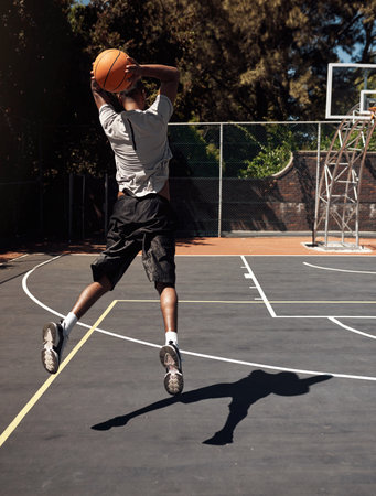 Shooting is the most important skill in basketball. Rearview shot of a sporty young man throwing a basketball into a net on a sports court.の写真素材