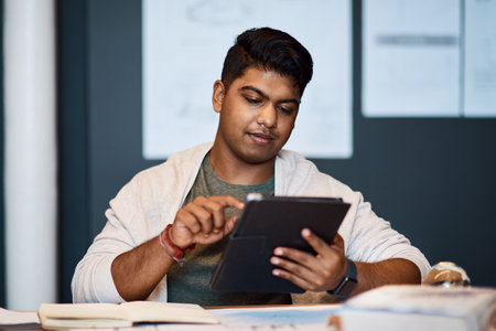 Cutting edge tech for cutting edge building designs. a young architect using a digital tablet while drawing up a building plan.の写真素材