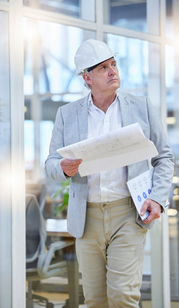 Mature man, blueprint and construction manager walking in building site, project management and design. Engineering, contractor and thinking of floor plan for architecture, development and innovationの写真素材