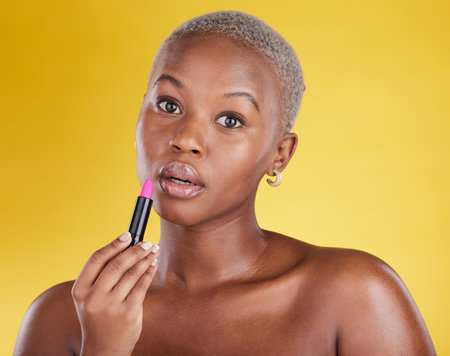 Face portrait, makeup and black woman with lipstick in studio isolated on a yellow background. Cosmetics, beauty and African female model with lip gloss product for aesthetics, wellness and skincare.の写真素材