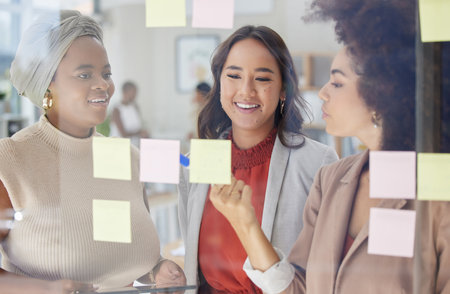 Mixed race businesswoman with afro using visual aid to brainstorm in office. Hispanic professional standing and writing while showing team of colleagues. Sharing ideas and planning marketing strategyの写真素材