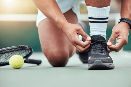Closeup of unknown indian tennis player getting ready and tying shoelaces on court. Ethnic fit athlete kneeling alone before playing match. Sporty man preventing injury and tripping in sports gameの写真素材