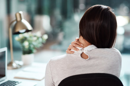 Trying to massage the pain away. Rearview shot of a young businesswoman experiencing neck pain while working in an office.の写真素材