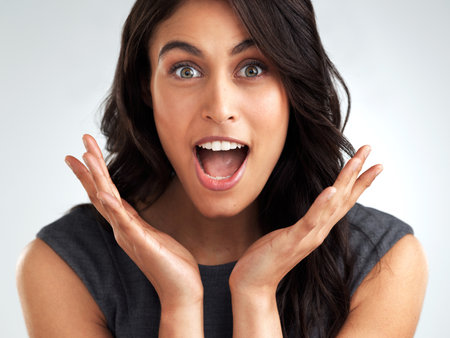 This will come as a surprise to you. a young woman looking surprised while posing against a white background.の写真素材