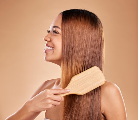 Beauty, woman and brush hair for growth and shine for straight texture on a brown background. Smile of aesthetic female happy in studio brushing for natural keratin treatment haircare resultsの写真素材