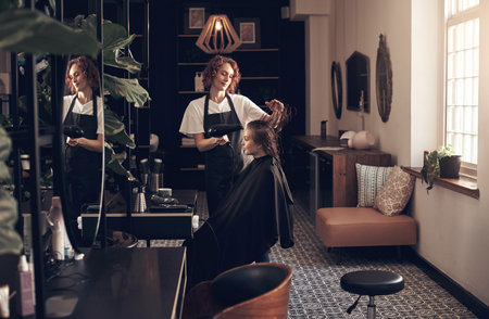We style your hair however you want it. a woman blowdrying her clients hair in her salon.の写真素材