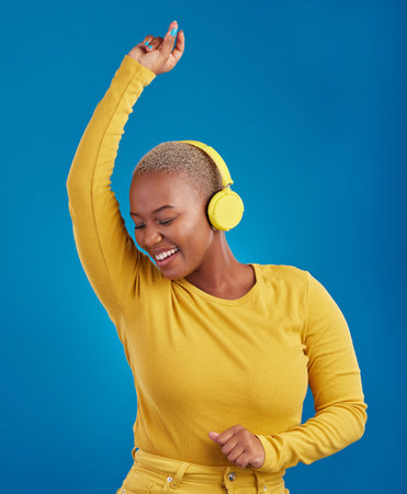 Black woman with headphones, dancing and listening to music, rhythm and fun with freedom on blue...