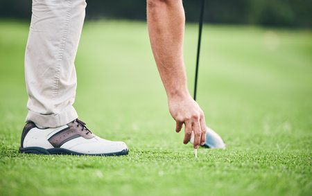 Sports, golf ball and tee with hand of man on course for training, tournament and challenge. Start, competition match and ready with athlete and club on grass field for action, games and hobbyの写真素材