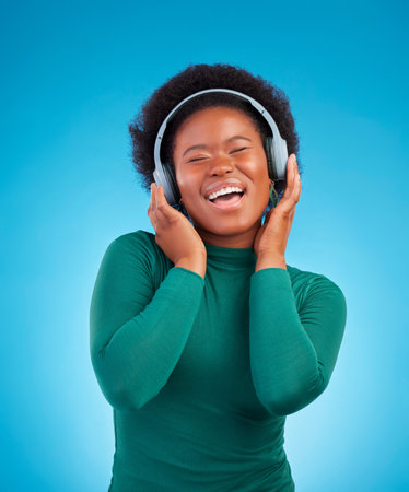Happy, music and headphones with black woman in studio for streaming, singing and relax. Online radio, technology and listening with female isolated on blue background for hip hop and subscriptionの写真素材
