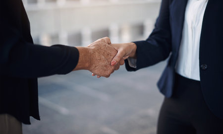Deal with people who get thing a done. Cropped of two businesswomen shaking hands against a city background.の写真素材
