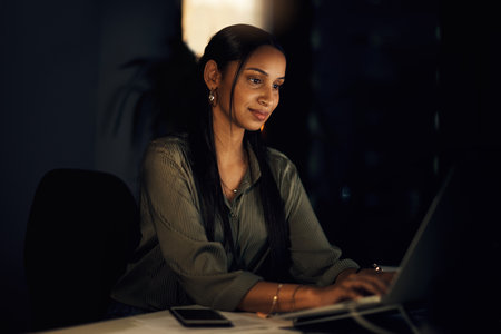 Wide awake and still very productive. a young businesswoman working on a laptop in an office at night.の写真素材