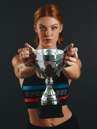 Success isnt given, its earned. Studio portrait of a sporty young woman holding a trophy against a black background.の写真素材