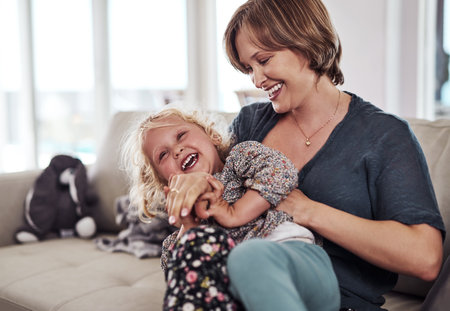 Shes always been so ticklish. an attractive young mother sitting and tickling her daughter during a day at home.の写真素材