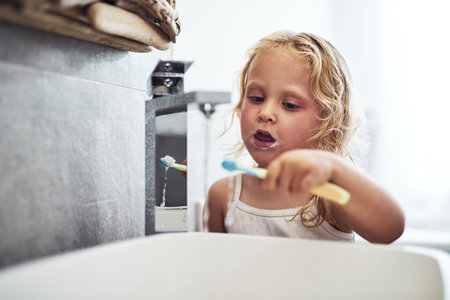 I can do this all alone. an adorable little girl standing alone and brushing her teeth during her morning routine at home.の写真素材