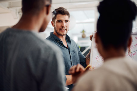 Visualising ideas goes a long way in business. a diverse group of businesspeople standing together and using a visual aid to brainstorm in the office.の写真素材