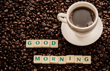 May your mornings be brew-tiful. Closeup shot of a cup of coffee and block letters forming the words good morning on a pile of coffee beans.の写真素材